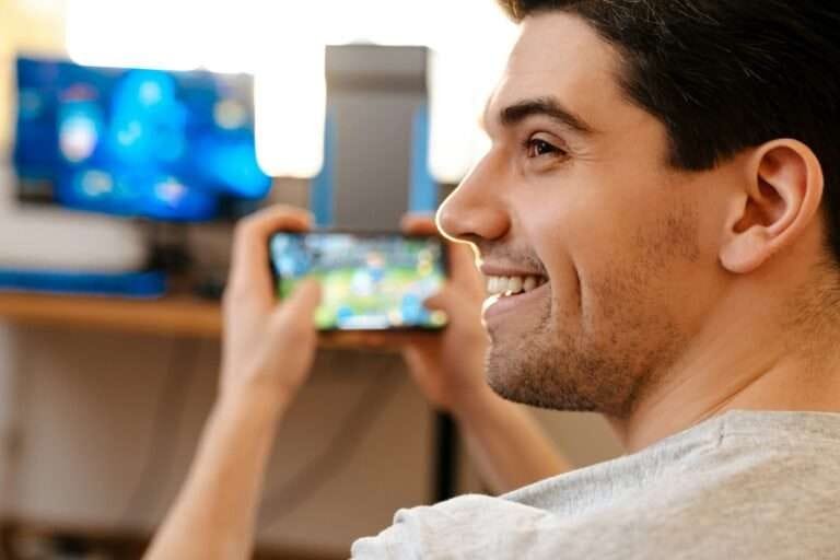 Happy brunette guy playing video game on his mobile phone